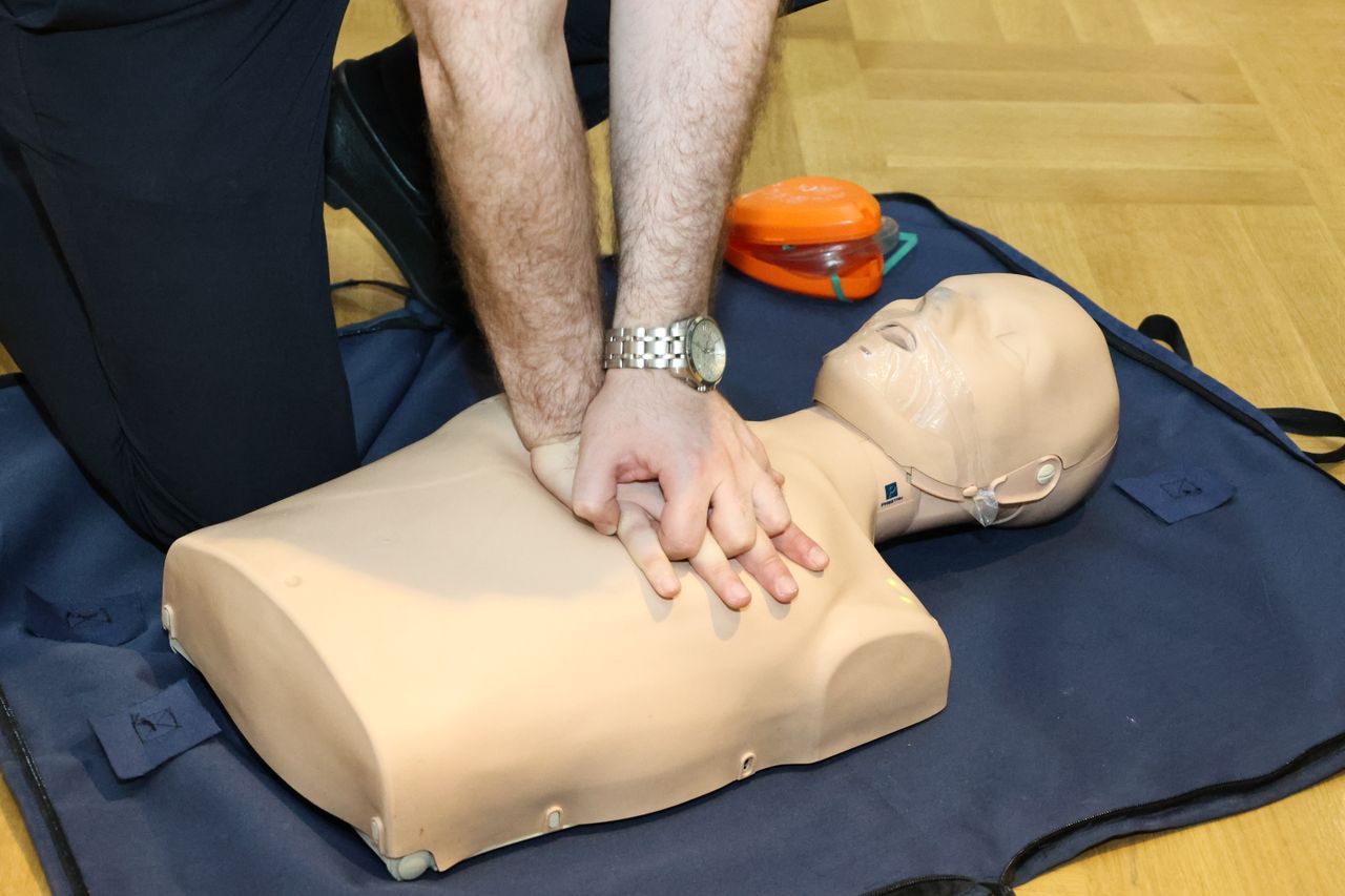Healthcare professional performing CPR training on a medical manikin during multilingual medical device and emergency response instruction.